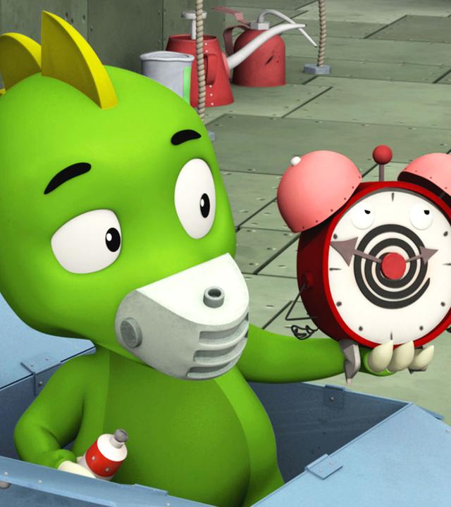 Koks steht in einem Pappkarton und hält einen Wecker in der Hand.