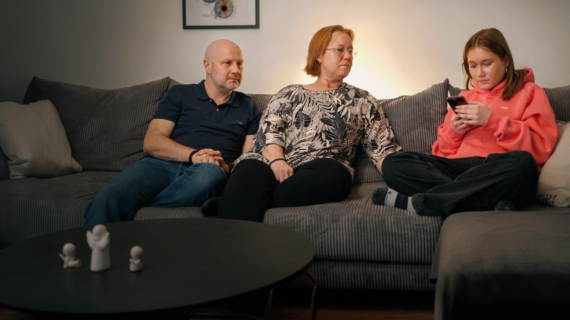 Paulina (16) sitzt mit ihren Eltern auf dem Sofa und schaut auf ihr Smartphone.