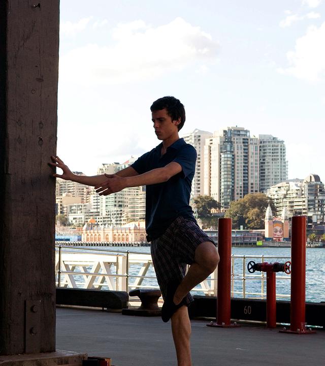 Sammy tanzt Ballett im Freien, hinter ihm sieht man Wasser und moderne Gebäude.