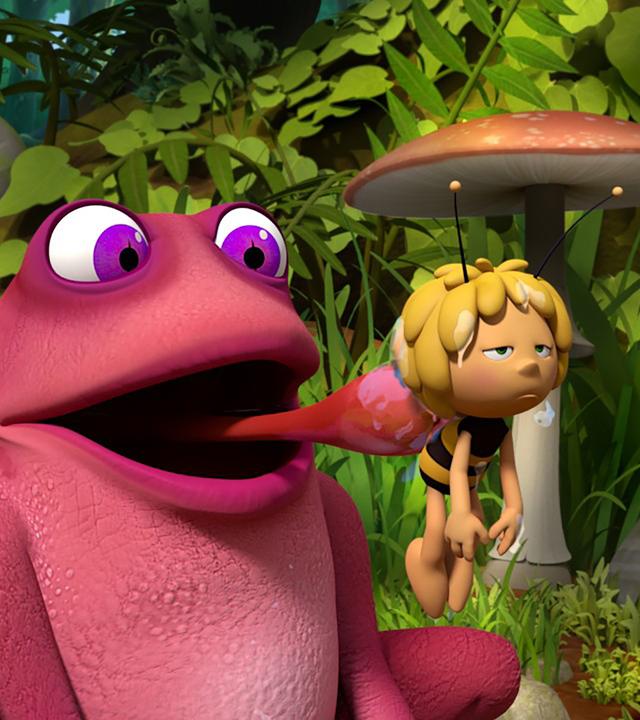 Kröte Rosalie schlabbert Biene Maja mit der Zunge ab. Willi und Walter fliegen vor Maja.