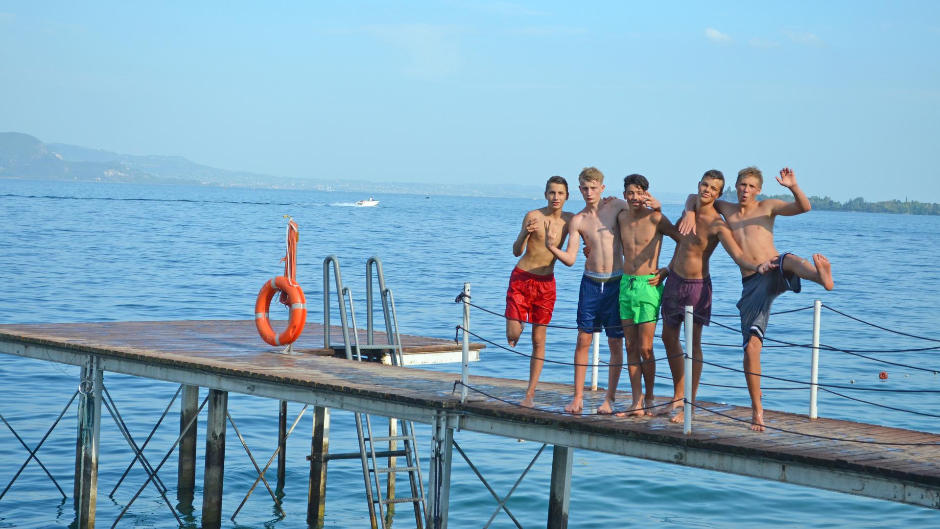 Die Jungs stehen in Badehose auf dem Steg.