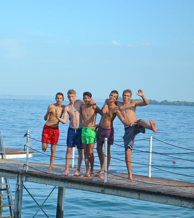 Die Jungs stehen in Badehose auf dem Steg.