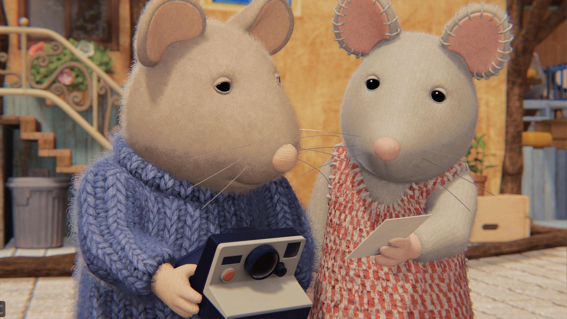 Sam und Julia stehen nebeneinander und schauen gemeinsam auf ein Foto, das Julia mit der linken Hand hochhält. Sam hält eine Polaroidkamera in beiden Händen.  Beide stehen in einem gepflasterten Hof vor einem Gebäude.