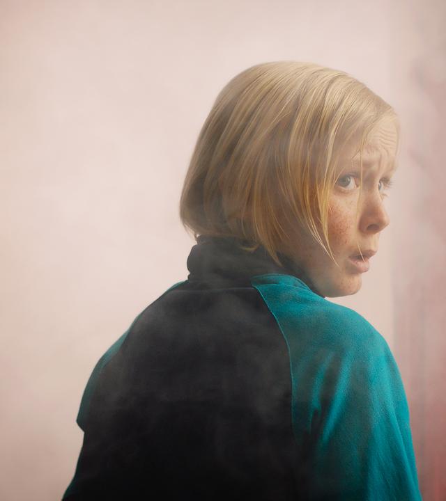 Raymond  schaut mit ängstlichem Blick über seine rechte Schulter nach hinten. Vor ihm ist eine geöffnete Tür zu sehen aus der Nebel steigt.