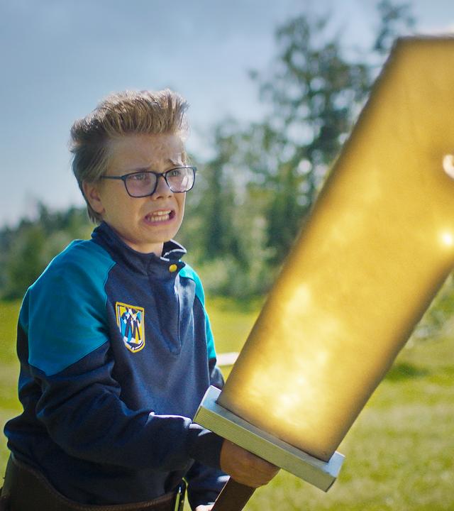 Uno steht mit ängstlichem Blick auf einer Wiese, die von Bäumen und Sträuchern umringt ist. Er hält angestrengt ein riesiges golden leuchtendes Schwert mit beiden Händen fest. Im Hintergrund stehen Zielscheiben.
