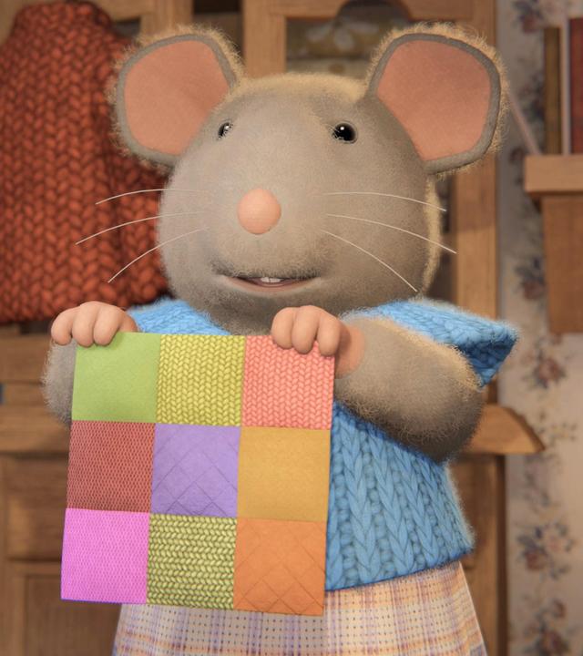 Sams Mutter steht im Kinderzimmer zwischen den Kinderbetten und hält ein buntes Patchwork-Viereck hoch.