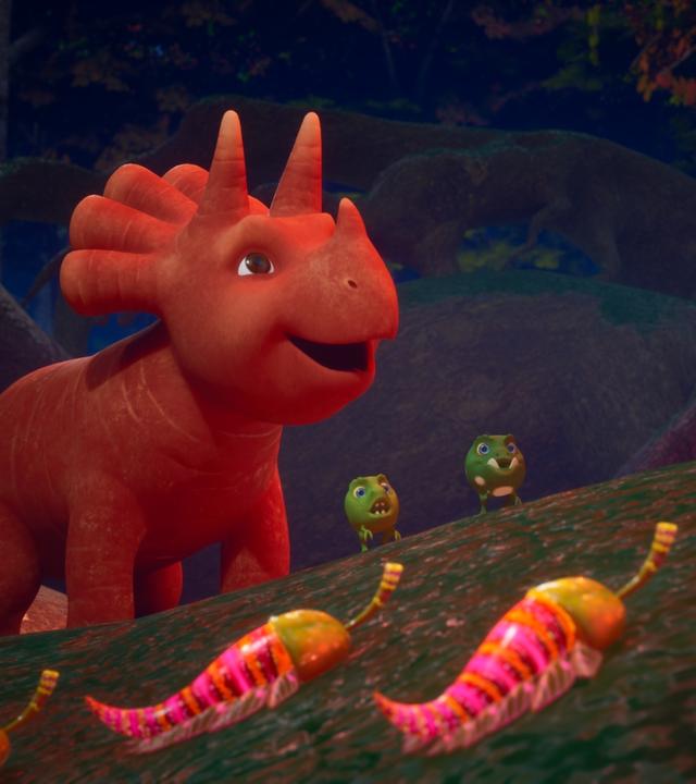 Ginger und ihre Erbs-Rex-Freunde laufen durch einen nächtlichen Wald. Sie stehen staunend vor leuchtenden Wesen, die aussehen wie Chilis mit kleinen Beinchen. Ginger ist ein Saurier-Mädchen, das einer Karotte ähnelt, Erbs-Rexe sehen Erbsen ähnlich.