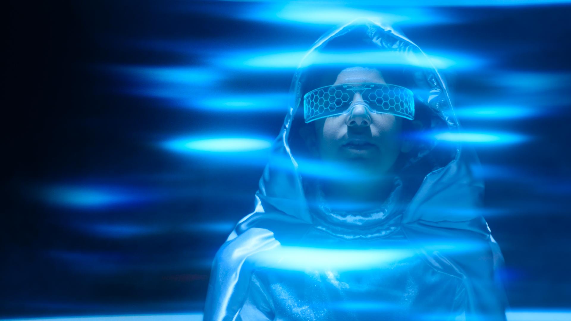 Bekleidet mit einem silbernen Weltraumanzug und spaciger Brille und umringt von blauen Strahlen, steht der neue Austauschschüler Juan da und schaut mit mystischem Blick nach vorne.