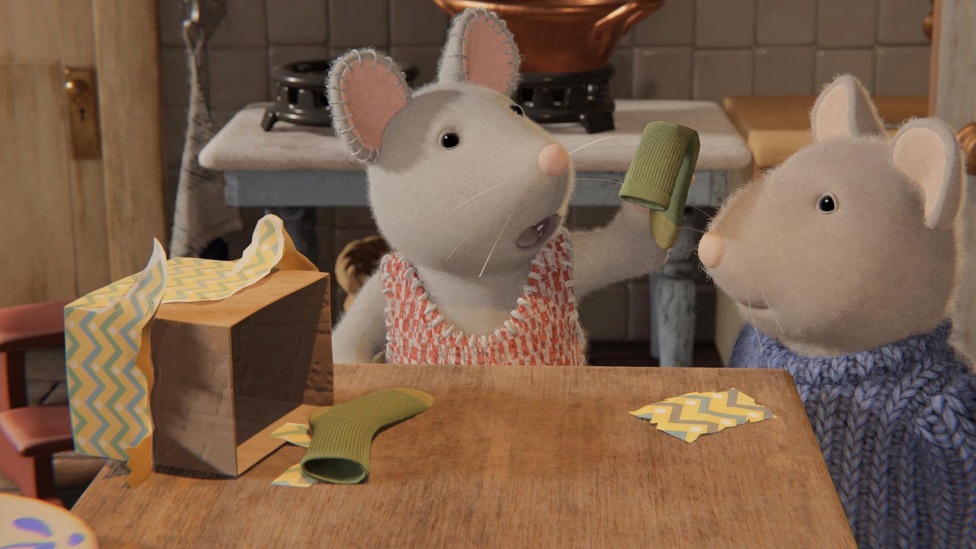 Julia und Sam stehen vor einem Holztisch in der Küche. Julia hält eine grüne Socke hoch, eine weitere liegt neben einem aufgerissenen Paket. Julia schaut enttäuscht, Sam etwas nachdenklich auf die Socke.