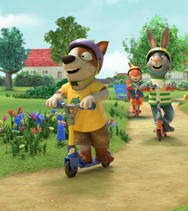 Draußen auf einem Weg im Park findet ein Rollerwettrennen statt. Ganz klar in Führung vorne liegt Zac, der Hund. Hinter ihm folgen Posy die Maus, Pip das Kaninchen und Jamila das Eichhörnchen. Alle lachen und tragen zum Schutz bunte Helme.