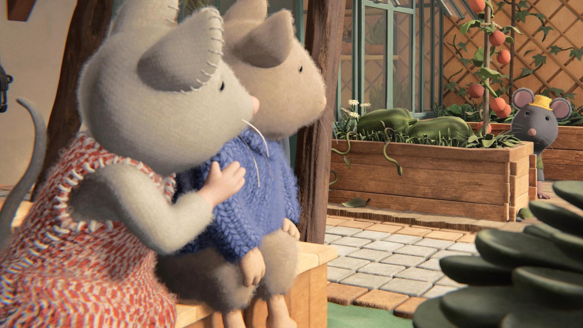 Julia und Sam sitzen nebeneinander auf einer Bank und schauen zu Tonio, der auf der anderen Seite des Hofes hinter einem Hochbeet sitzt. Neben Tonio steht ein Gewächshaus und hinter ihm ein weiteres Hochbeet. Dahinter hängt ein großes Rankgitter an der Wand.