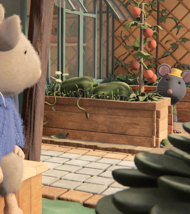 Julia und Sam sitzen nebeneinander auf einer Bank und schauen zu Tonio, der auf der anderen Seite des Hofes hinter einem Hochbeet sitzt. Neben Tonio steht ein Gewächshaus und hinter ihm ein weiteres Hochbeet. Dahinter hängt ein großes Rankgitter an der Wand.