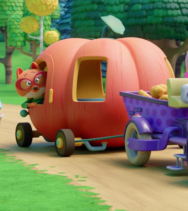 Die Füchsin Fiona sitzt in einem riesigen Kürbis, in den Fenster und eine Tür geschnitzt sind und an dem wie bei einem Auto unten Räder angebracht sind. Sie schaut aus der Fensteröffnung der Tür hinaus. Der Kürbis wird von einer Baumaschine gezogen, die von Schweinchen Cornelia gelenkt wird. Hinter dem Kürbis fährt Schweinchen Charlie auf einer weiteren Baumaschine mit, im rechten Hintergrund lenkt Schweinchen Caesar einen fahrbaren Bagger.