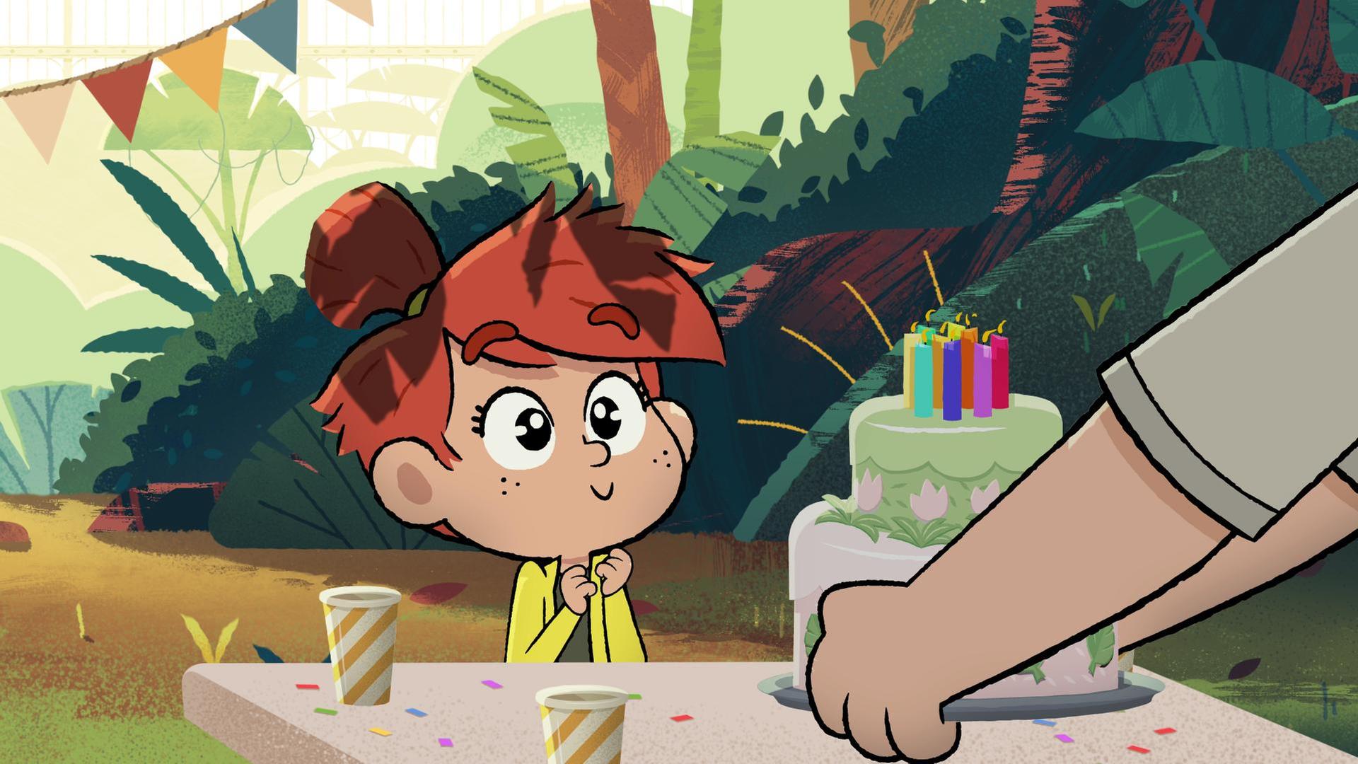 Ein Mädchen mit roten Haaren sitzt freudig aufgeregt im Dschungel an einem gedeckten Tisch und bekommt eine doppelstöckige Torte mit brennenden Kerzen gebracht.