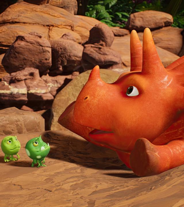 Ginger, das Sauriermädchen, das aussieht wie eine Karotte, steckt in einer Felsspalte fest. Vor ihr stehen vier kleine, grüne, runde Wesen - die sogenannten Erbs-Rexe. Sie schauen ein wenig hilflos.