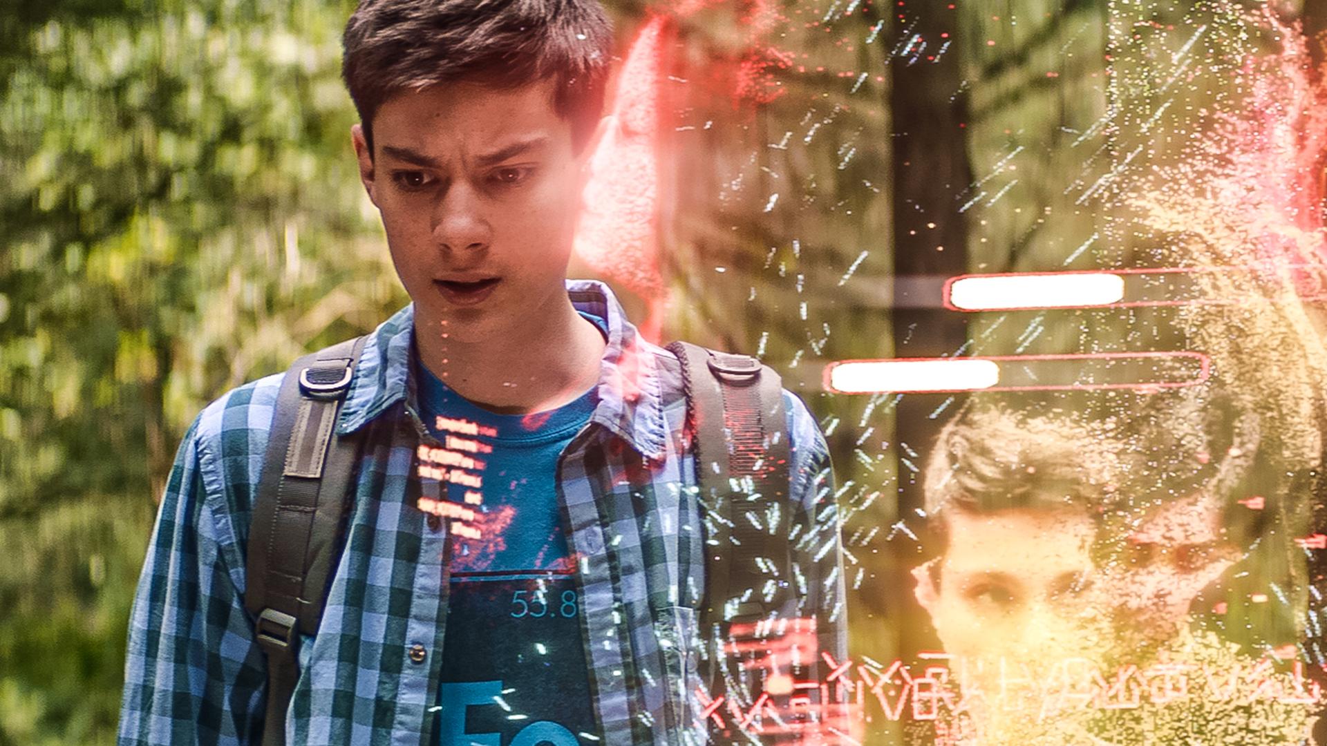Im Wald bei Tageslicht steht Louis mit ernstem Gesichtsausdruck neben einem transparenten Band, in dem sein Hologramm zweimal deutlich zu sehen ist. Kaz und Megs Hologramme sind zu erahnen. Zwei weiße Fortschritts-Balken sind über Louis Kopf im transparenten Band.