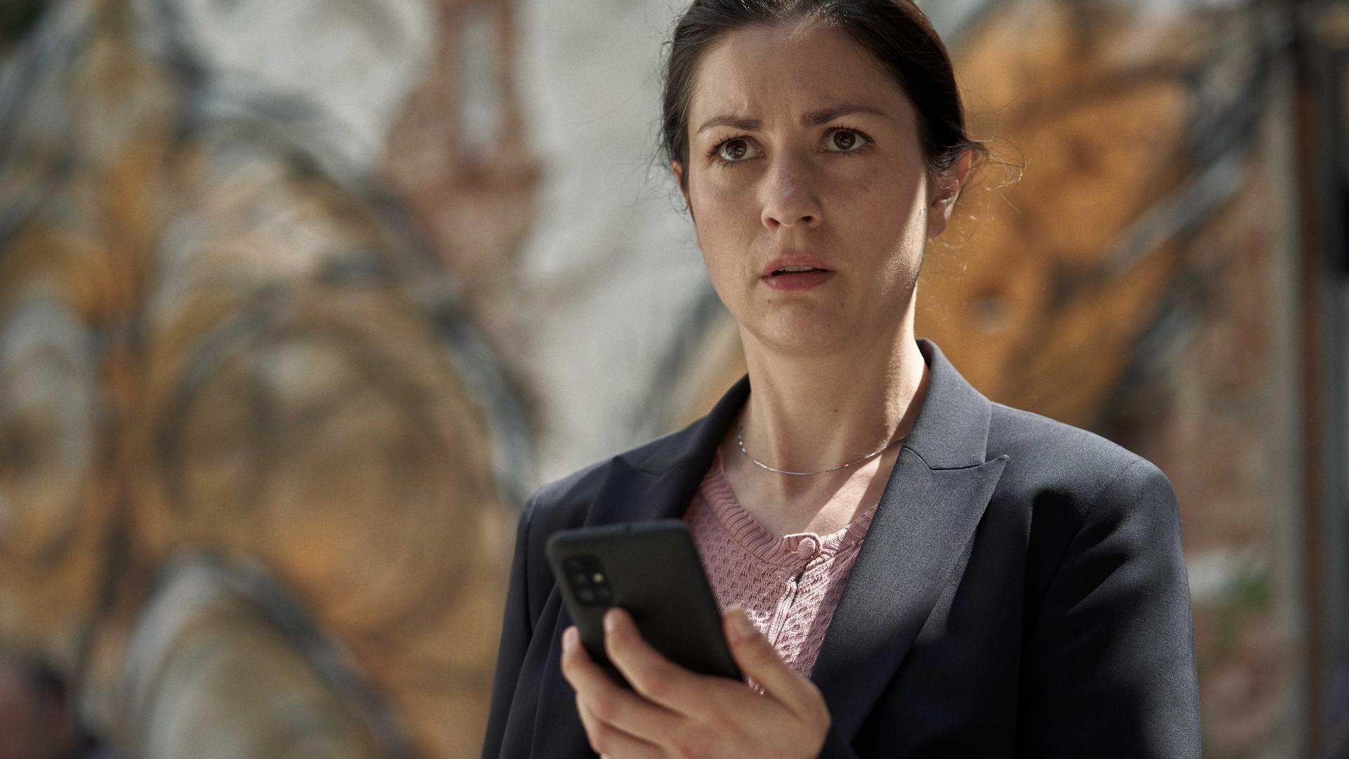 vera (Eva Meckbach) schaut auf ihr Handy.