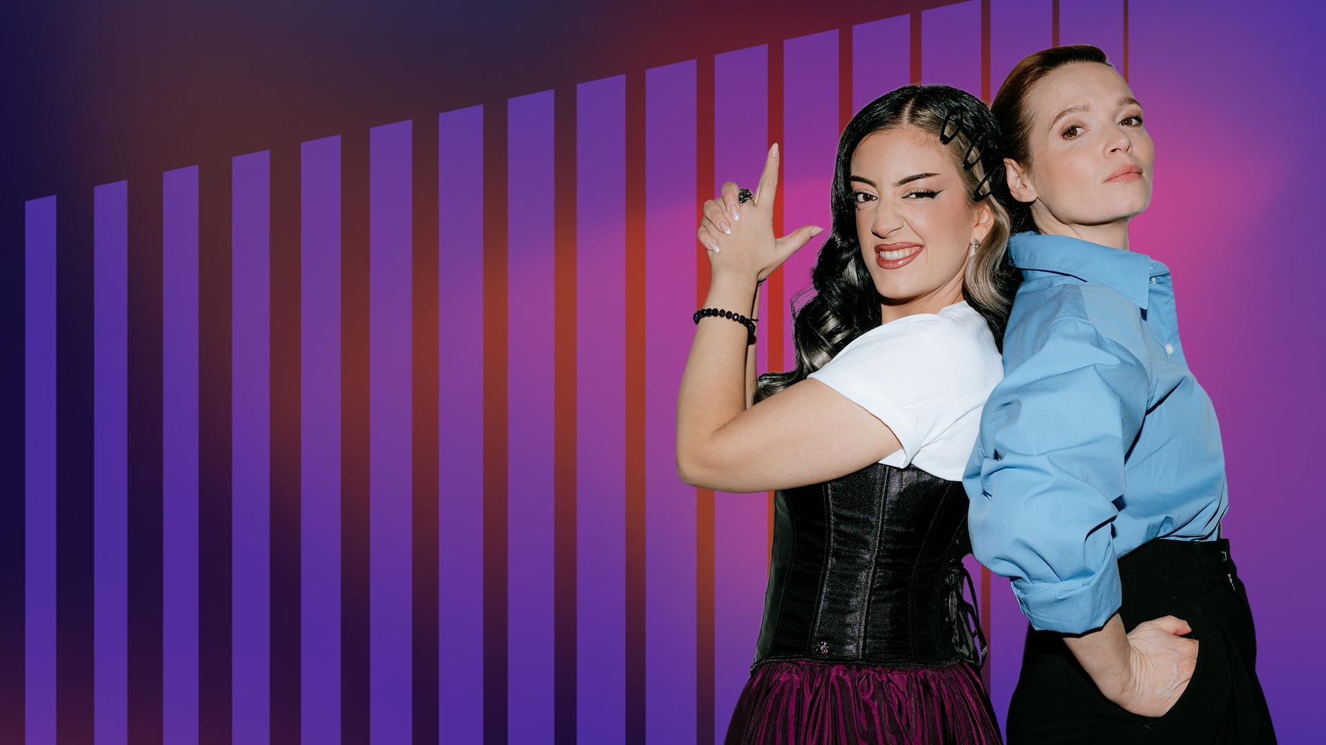 Parshad und Karoline Herfurth stehen Rücken an Rücken und Parshad simuliert mit den Händen eine Pistole.