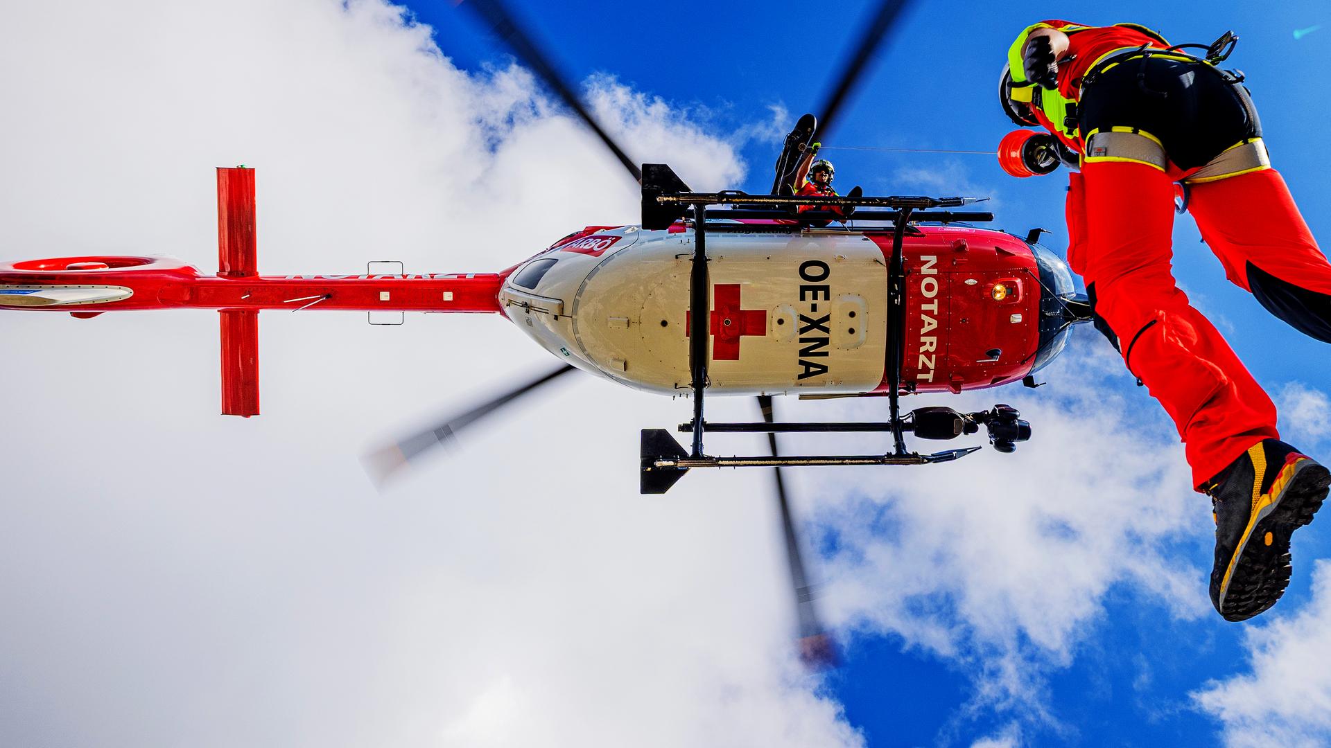 Ein Flugretter wird mittels Seilwinde von einem schwebenden Heli herabgelassen.