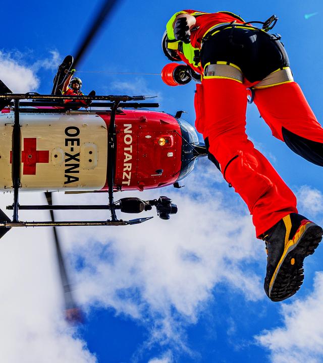 Ein Flugretter wird mittels Seilwinde von einem schwebenden Heli herabgelassen.