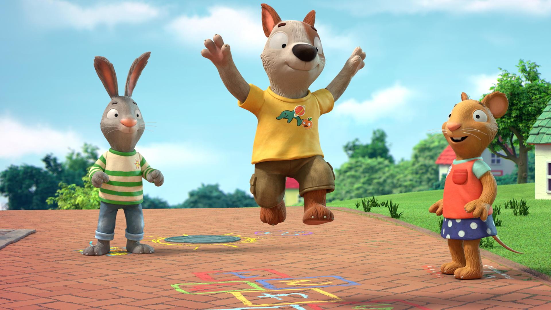 Auf einem gepflasterten Weg in einer Wohngegend zwischen Häusern spielen Pip, das Kaninchen, Posy, die Maus und Zac der Hund. Zac ist mitten im Spiel und gerade im Sprung. Mit bunter Kreide ist das Hüpfspiel Himmel und Hölle auf den Weg gemalt.