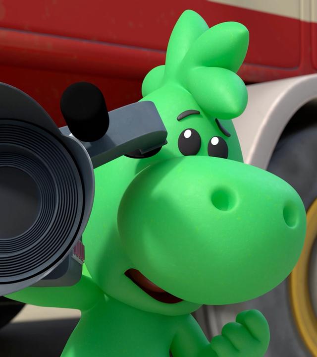 Grisu, der kleine grüne Drache, hält eine große Filmkamera in der Hand. Er steht vor einem Feuerwehrauto.