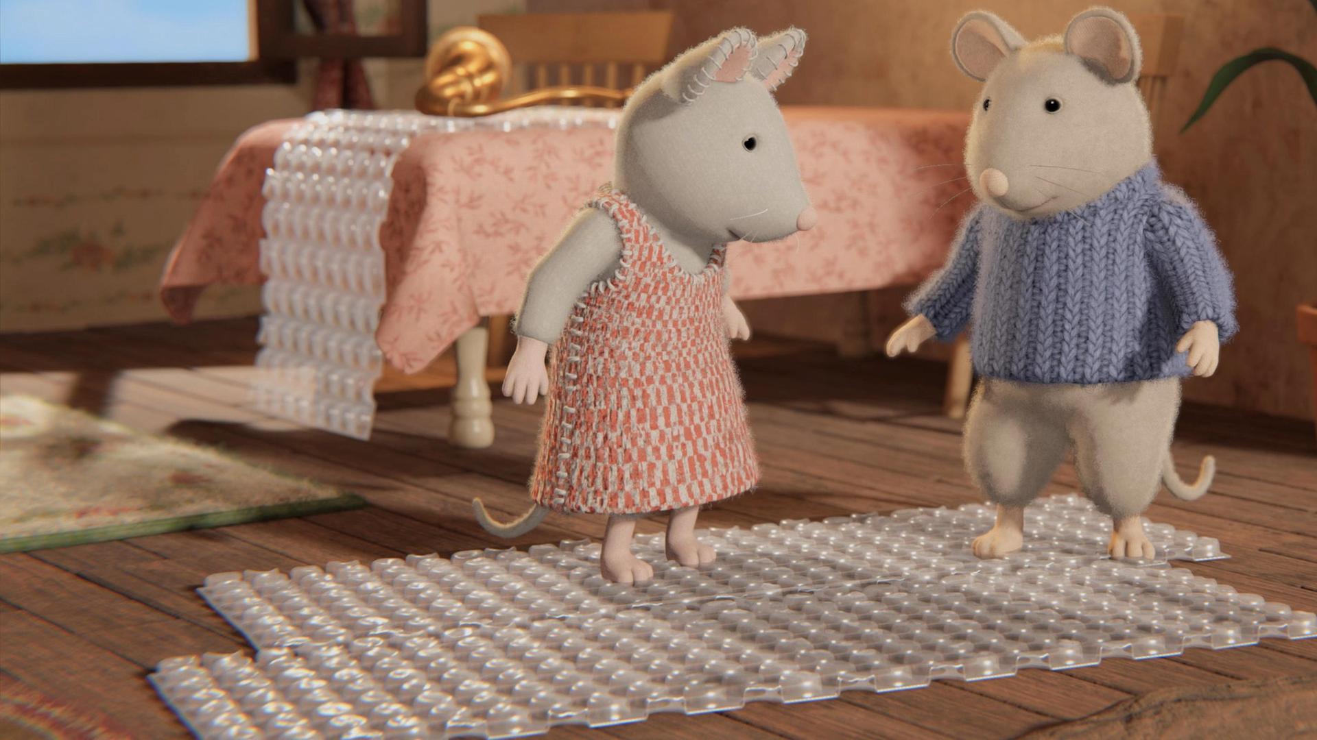 Julia und Sam stehen mit fröhlichen Gesichtern auf einer Luftpolsterfolie in der Wohnung von Oma Gouda. Sie scheinen die Blasen mit den Füßen zu zerdrücken. Hinter ihnen auf einem Tisch liegt eine weitere Folie und darauf liegt ein Hörrohr.