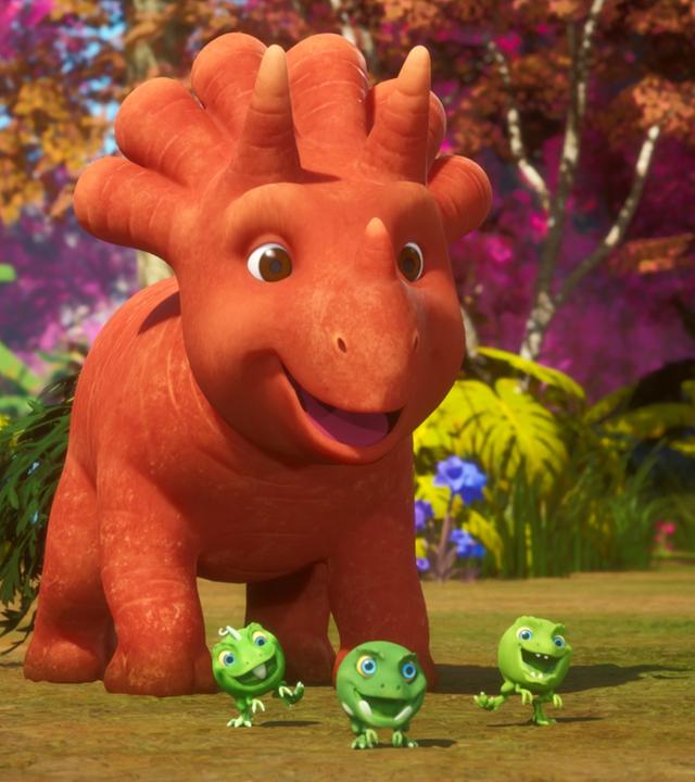 Das orangefarbene Trikarottops-Mädchen Ginger und ihre drei grünen Erbs-Rex-Freunde stehen in der Mitte des Bildes und lachen und freuen sich. Im Hintergrund ist ein bunter Wald zu sehen.