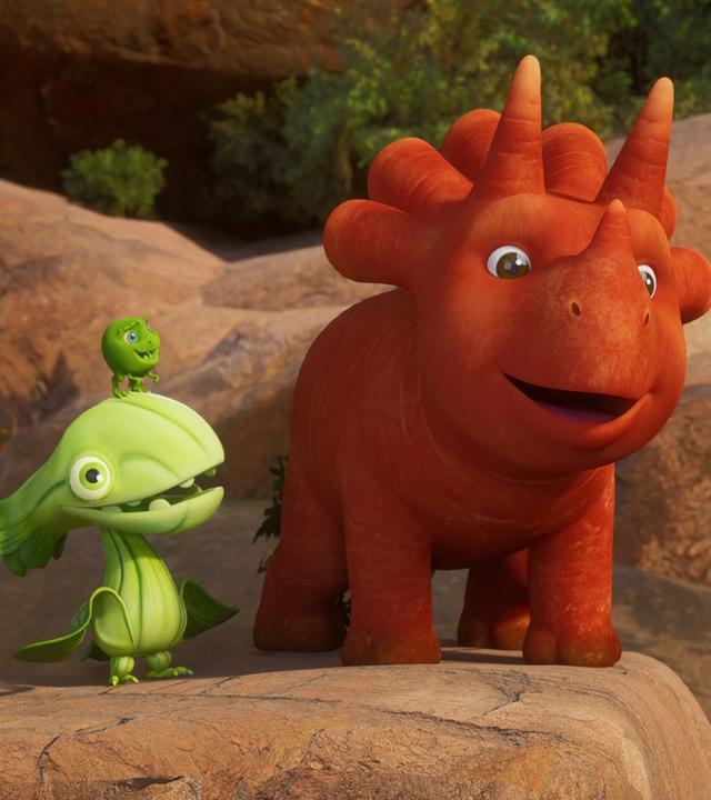 Auf einem erhöhten Felsen stehen Ginger, das Trikarottops-Mädchen und ein Pakchoidactylus. Auf dem Kopf des Asia-Kohl-Vogels sitzt ein Erbs-Rex. Sie schauen beide Ginger an - und Ginger macht ein fröhliches Gesicht.