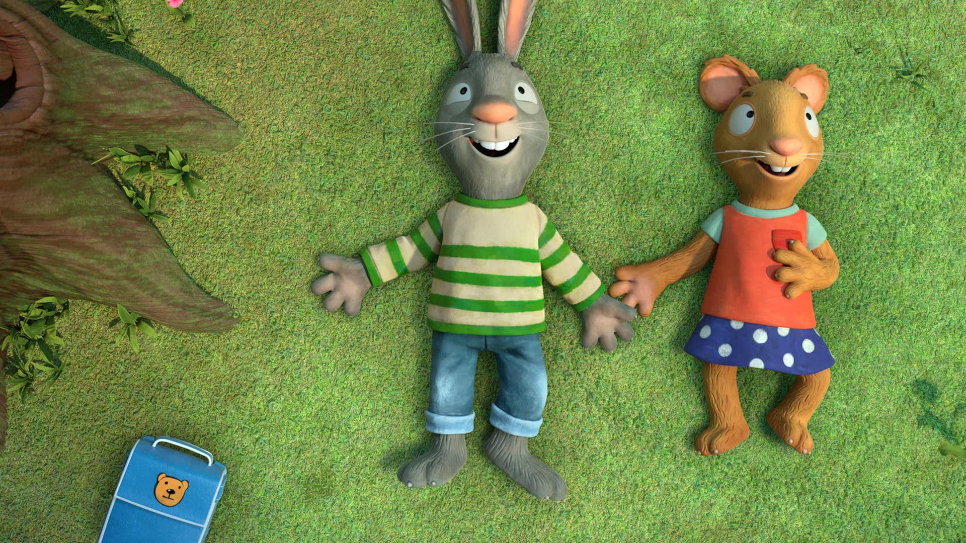 Pip, das Kaninchen und Posy, die Maus liegen nebeneinander auf einer Wiese, schauen nach oben und lächeln glücklich.