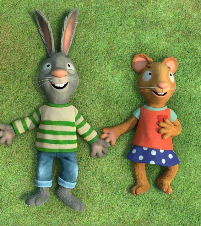 Pip, das Kaninchen und Posy, die Maus liegen nebeneinander auf einer Wiese, schauen nach oben und lächeln glücklich.