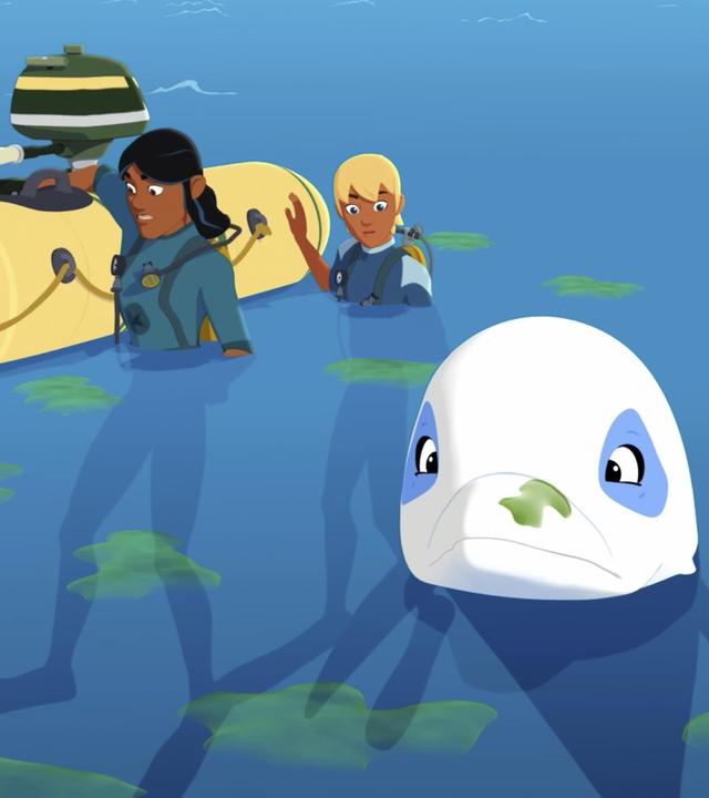 Auru und Yann sind mit Taucheranzügen im Meer und halten sich an einem Schlauchboot fest. Delfin Zoom schwimmt vor ihnen im Wasser, auf dem grüne Flecken an der Wasseroberfläche zu sehen sind.