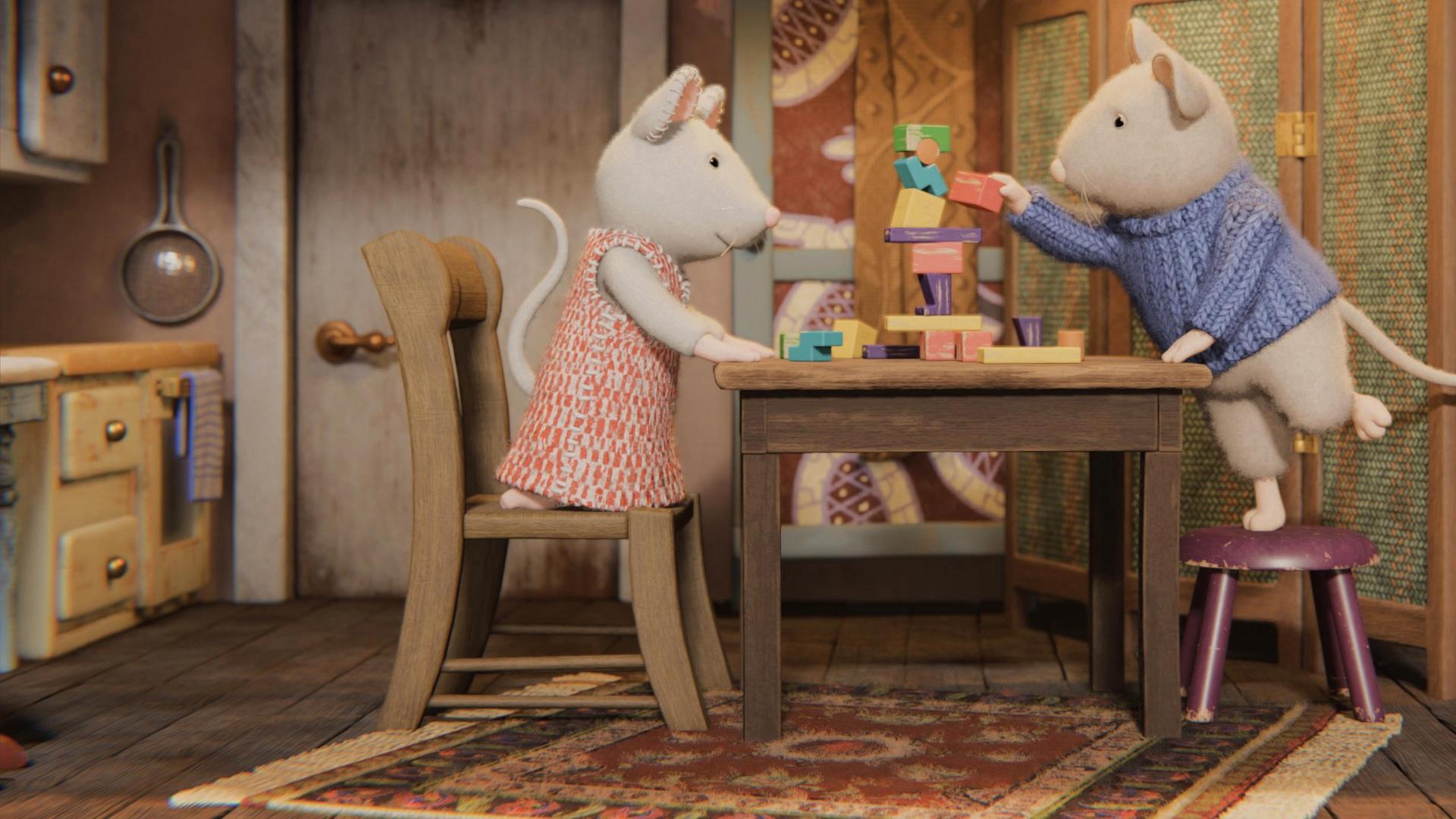 Julia kniet auf einem Stuhl an einem Tisch, Sam steht auf einem Hocker an diesem Tisch. Sam stellt gerade ein rotes Holzklötzchen auf einen Turm aus bunten Holzklötzchen. Julia schaut ihm aufmerksam dabei zu. Die beiden befinden sich in einem gemütlichen Zimmer des Mäusehauses. Rechts steht ein Bett hinter einem Paravent, links befindet sich eine Küchenzeile. Im Hintergrund sind eine Tür und ein Schrank zu sehen.