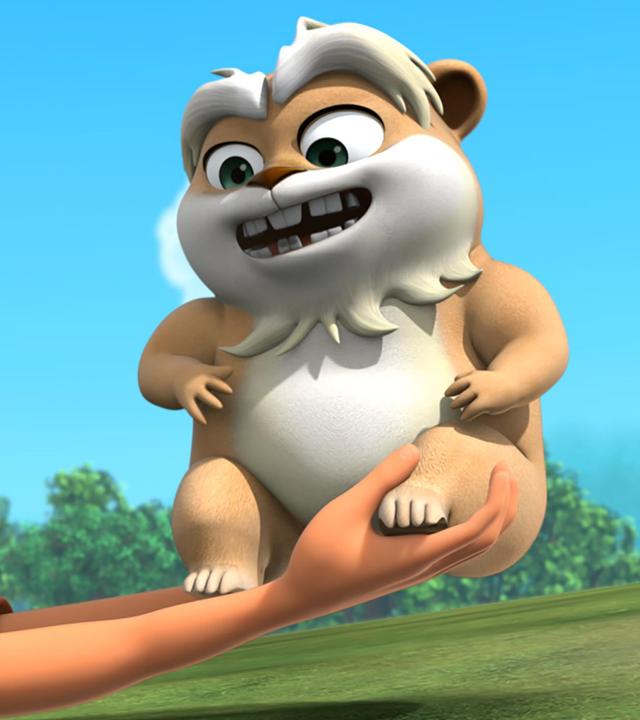 Scarlett liegt auf dem Bauch vor blauem Himmel auf einer grünen Wiese und hält Hamster Derke in ihren nach vorne ausgestreckten Händen. Beide lachen fröhlich.