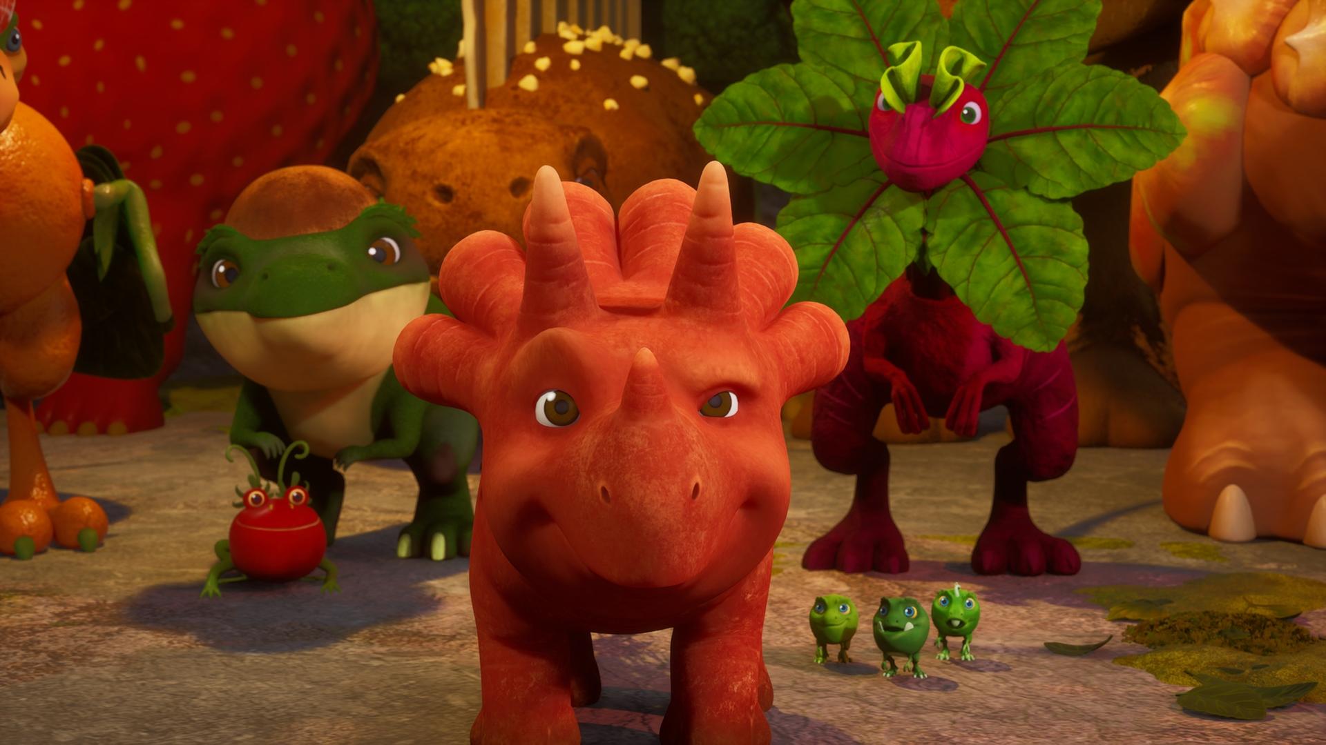 Das Trikarottops-Mädchen Ginger (es sieht aus wie eine orangefarbene Karotte mit Gesicht und Beinen.) steht in der Bildmitte und schaut nach vorne. Um sie herum stehen viele Vegesaurier dicht an dicht: Ein Avocadodon, ein Rotrüben-Saurier, ein Tomatodon, die Erbs-Rexe und noch viele weitere etwas im HIntergrund.