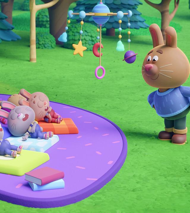 Auf einer lilafarbenen Picknick-Decke schlafen sechs kleine Hasen. Sie liegen mit geschlossenen Augen und offenen Mündern auf bunten Matratzen. Über ihnen - am Ast eines Baumes - hängt ein Mobile. Das Ganze schaut sich Papa Rüdi auf der Seite stehend an und scheint glücklich, dass seine Häschen eingeschlafen sind.