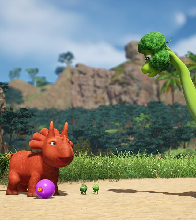 Ginger, das orangefarbene Trikarottops-Mädchen, hat einen violetten Fußball am Fuß. Sie scheint den Ball zu einem großen, grünen Brokkolisaurier kicken zu wollen, der ihr gegenüber steht. Mit dabei stehen die drei kleinen Erbs-Rexe.