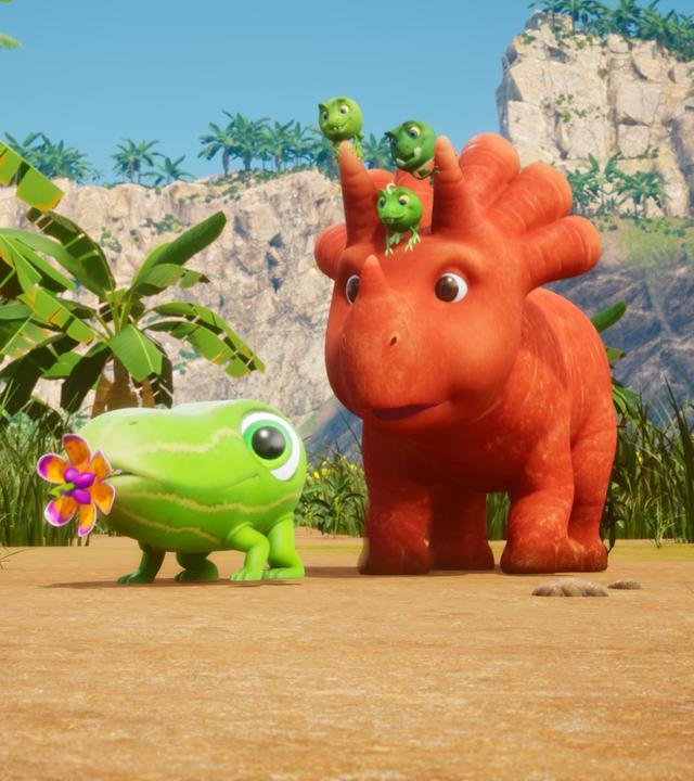 Eine kleine Gurke mit großen Augen und vier Füßchen - ein sogenanntes Gurkodil - hat einen bunten Blumenschnuller im Mund. Hinter ihm läuft Ginger, ein Saurier der aussieht wie eine Karotte mit Gesicht. Sie laufen am Strand, im Hintergrund stehen Palmen und Gräser.