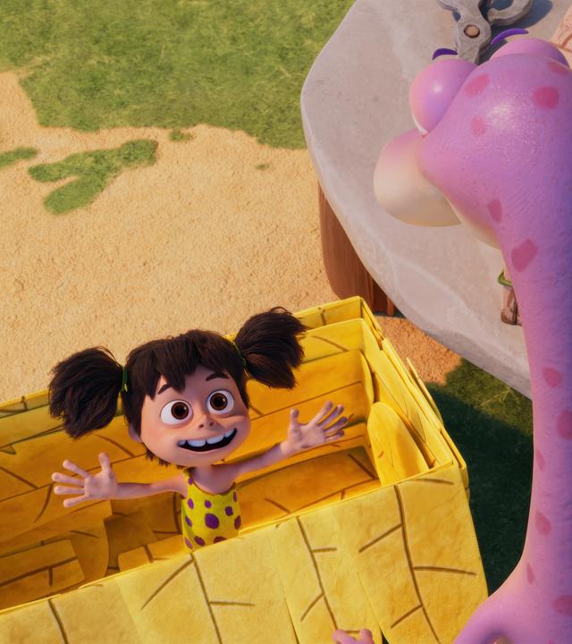 Das Urzeitmädchen Lucy steht mit ausgebreiteten Armen in einer gelben Pappkiste. Minus Drei - mit dem Rücken zu uns - betrachtet seine Freundin in der Kiste.