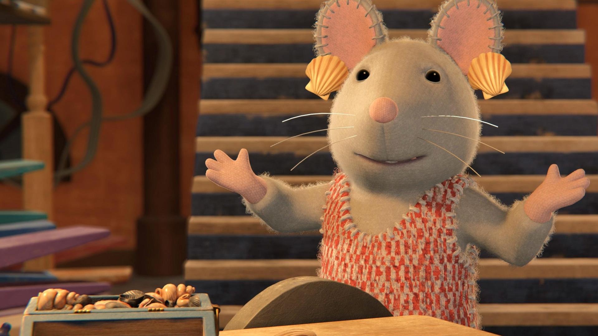 Julia steht mit ausgebreiteten Armen in einem Raum vor einem Tisch, auf dem eine kleine Holzkiste steht, in der Muscheln liegen. Neben der Kiste liegen ebenfalls ein paar Muscheln. Hinter Julia führt eine steile Treppe nach oben. Julia hat sich aus Spaß Muscheln als Ohrringe an die Ohren gehängt.