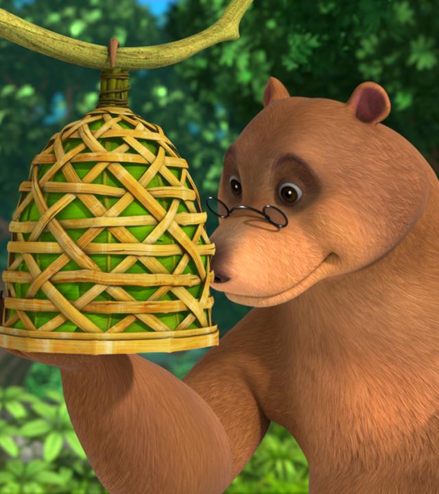 Balu sieht seinen selbstgebastelten Vogelkäfig an. In der linken Hand hält er rote Beeren.