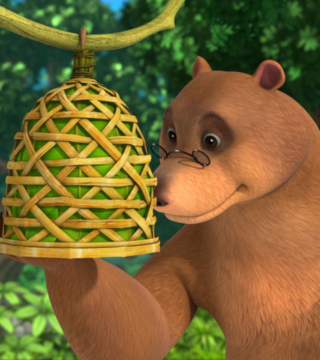 Balu sieht seinen selbstgebastelten Vogelkäfig an. In der linken Hand hält er rote Beeren.