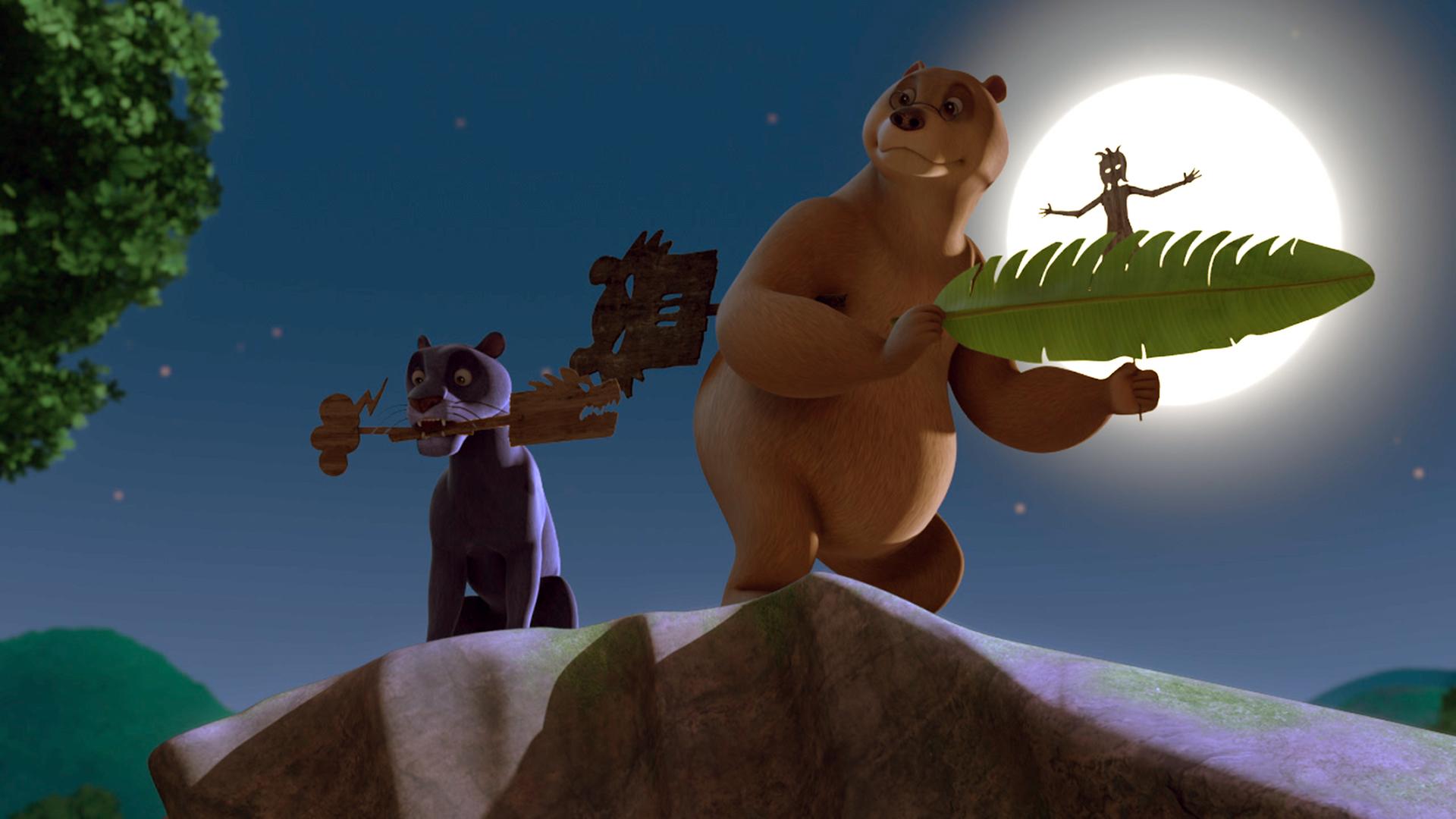 Baghira hält eine Holzfigur im Mund. Balu hat eine Figur unter den rechten Arm geklemmt und hält mit beiden Vorderpfoten ein Bananenblatt und eine Figur fest. Hinter ihm scheint der Vollmond.