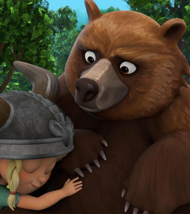 Auf einer Lichtung im Wald schmiegt sich die kleine Wikingerin Solveig liebevoll an den großen, braunen Bär Geri.