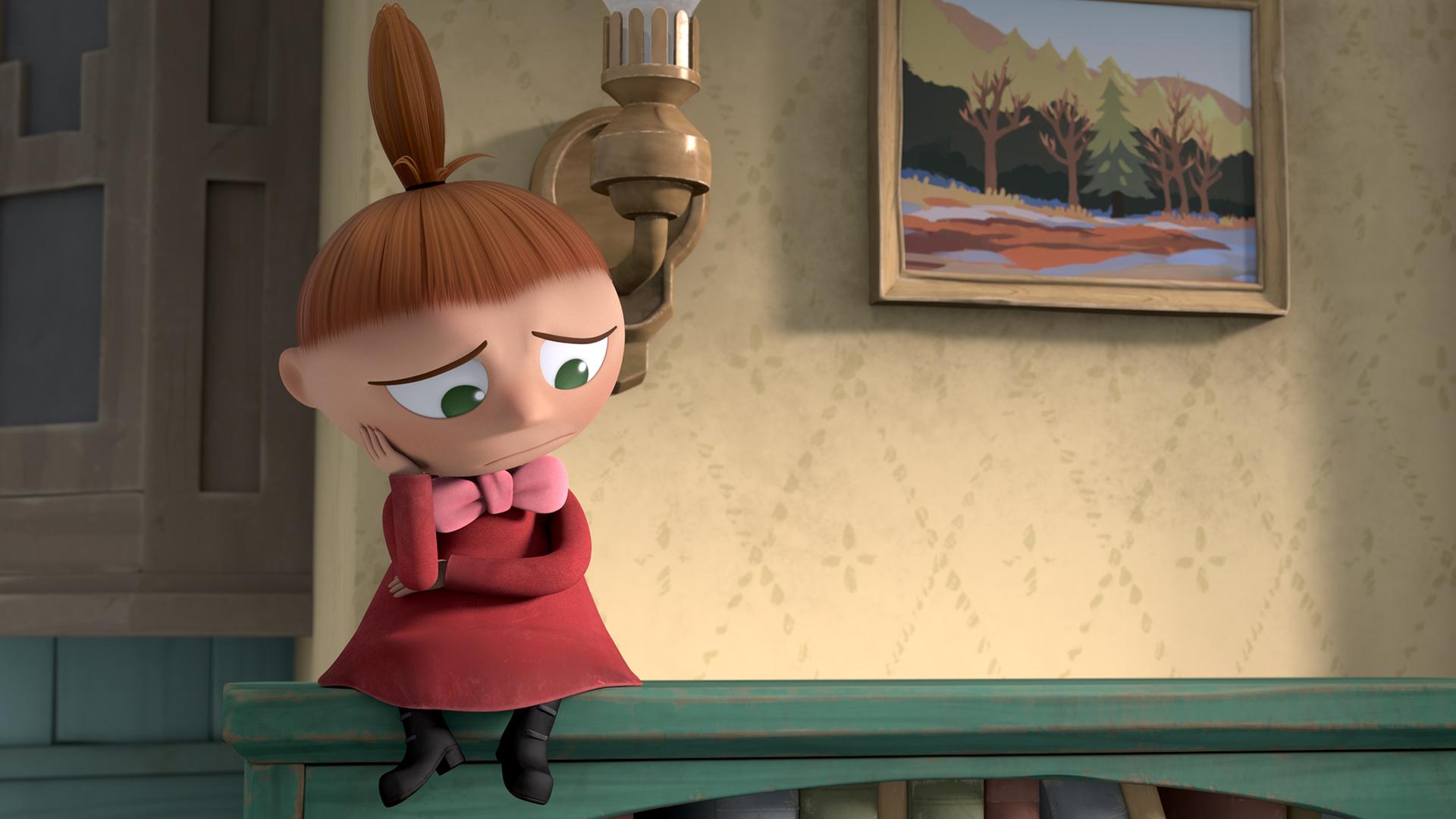 Die Kleine Mü sitzt allein auf einem Regal. Sie stützt ihren Kopf mit ihrer Hand und sieht sehr traurig aus.