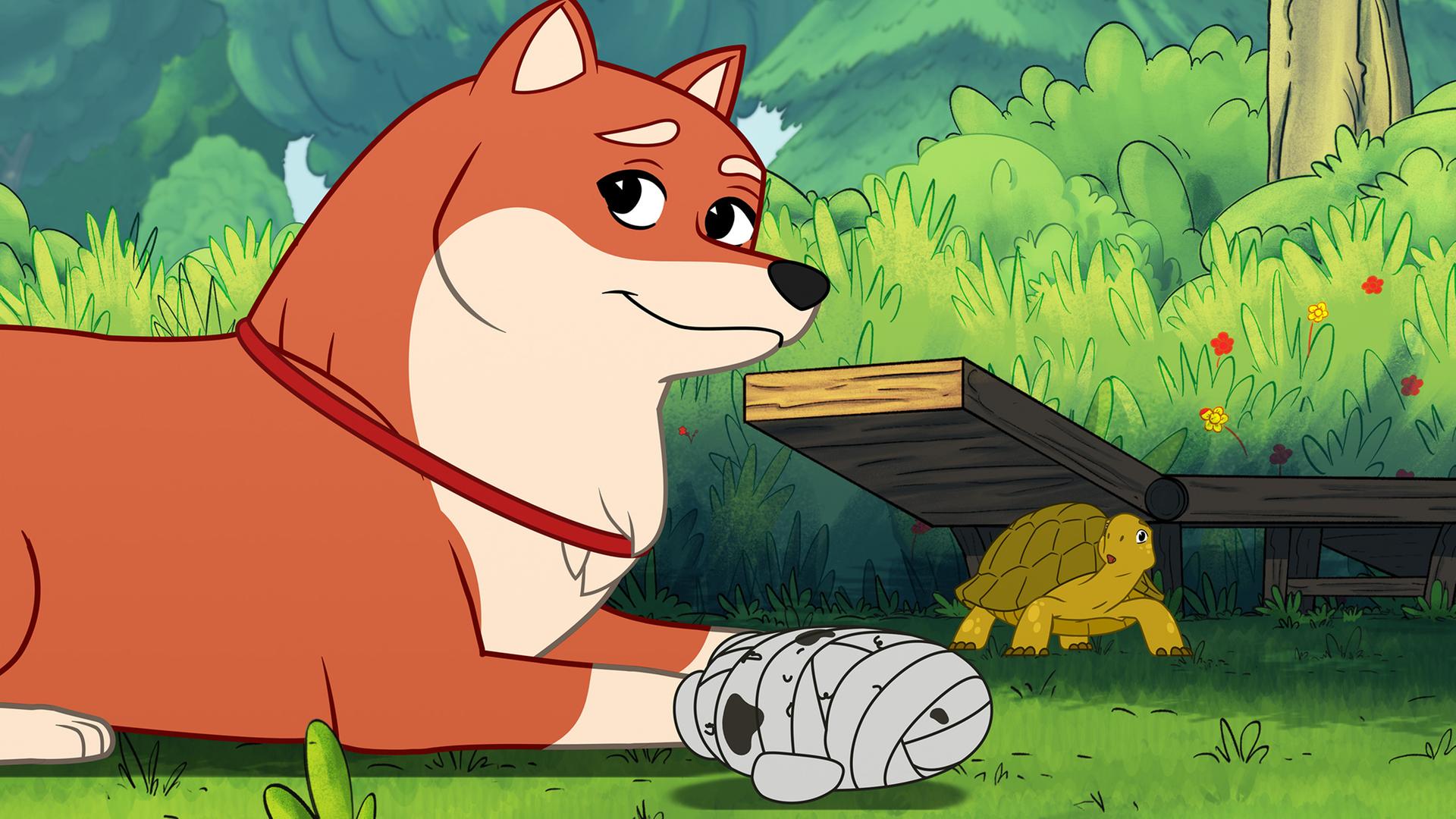 Die orangefarbene Hündin Nofretete, die einem Fuchs ähnlich sieht, liegt im Vordergrund auf dem grünen Gras und schaut zufrieden. Vor ihr ist ein Hundespielzeug in Form einer mit Verbänden umwickelten Mumie. Im Hintergrund steht die grüne Schildkröte Törtel mit erschrockenem Blick.