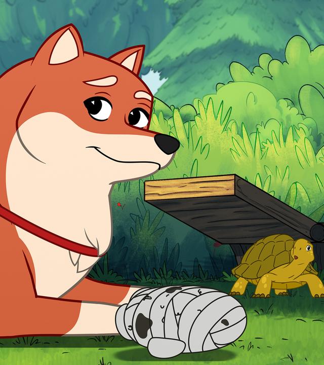 Die orangefarbene Hündin Nofretete, die einem Fuchs ähnlich sieht, liegt im Vordergrund auf dem grünen Gras und schaut zufrieden. Vor ihr ist ein Hundespielzeug in Form einer mit Verbänden umwickelten Mumie. Im Hintergrund steht die grüne Schildkröte Törtel mit erschrockenem Blick.