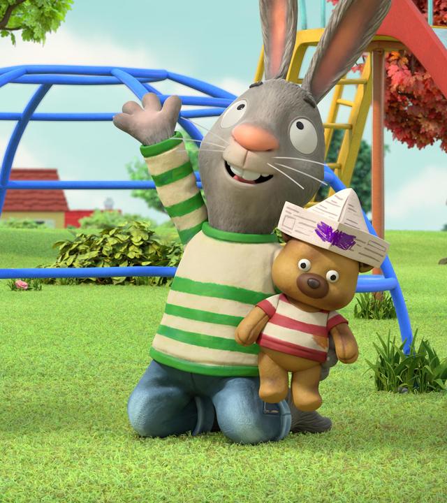 Draußen auf dem Spielplatz im Park knien Pip und Posy vor einem Klettergerüst und einer Rutsche auf der Wiese. Sie halten Stofftiere in den Händen, die aus Zeitungspapier gebastelte Piratenhüte tragen. Die Maus Posy hat ein rosafarbenes, vogelähnliches Stofftier und ihr bester Freund Pip, das Kaninchen einen Teddybären im Arm. Pip blickt nach oben Richtung Himmel und winkt mit seiner Hand.