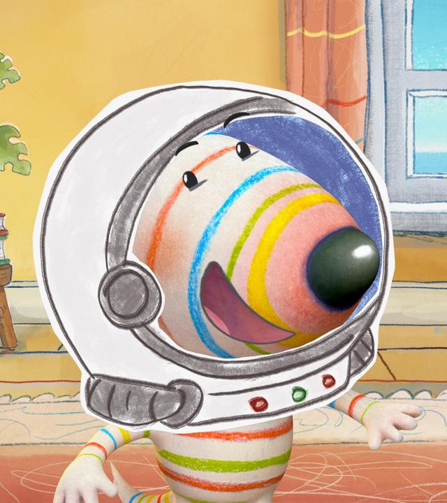 Hund Dylan steht in kompletter Astronautenmontur im Wohnzimmer. Er trägt einen Astronautenanzug mit Helm. Besonders auffällig ist ein großer, mechanischer Greifarm, den Dylan hochhält.
