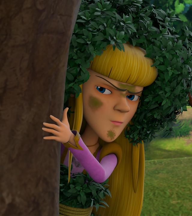 Nelly versteckt sich hinter einem Baum, hält sich mit der linken Hand am Stamm fest und beobachtet kritisch. Ihr Gesicht ist mit grünen Flecken beschmiert und sie trägt zur Tarnung Blätter auf ihrem blonden Haar.